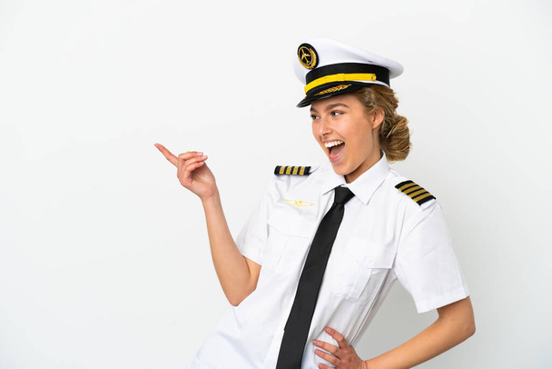Αεροπλάνο ξανθιά γυναίκα πιλότος απομονωμένη σε λευκό φόντο δείχνοντας το δάχτυλο στο πλάι και παρουσιάζοντας ένα προϊόν - Φωτογραφία, εικόνα