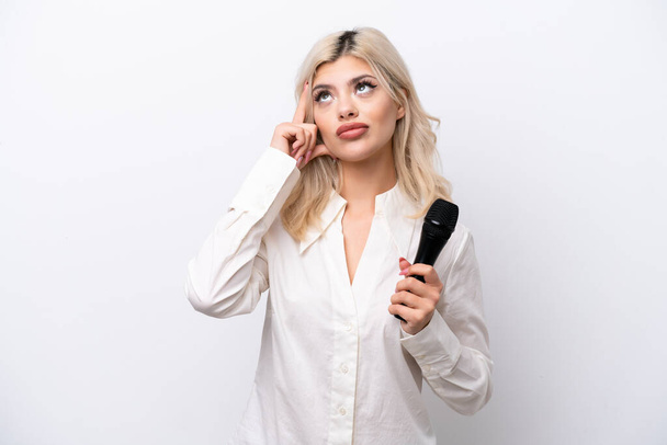 Genç şarkıcı kadın beyaz arka planda izole edilmiş bir mikrofonu alıp bir fikir düşünüyor. - Fotoğraf, Görsel