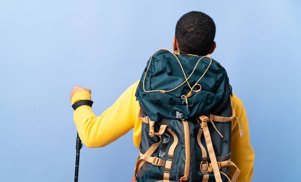 African American man with backpack and trekking poles over isolated background in back position - Photo, image