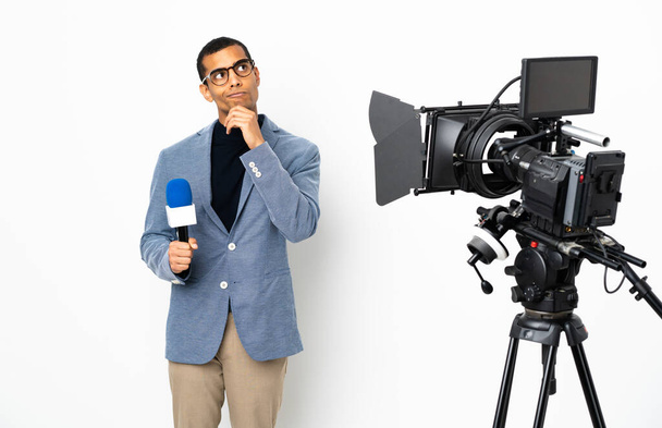 Reporter homme afro-américain tenant un microphone et rapportant des nouvelles sur fond blanc isolé penser une idée tout en levant les yeux
 - Photo, image