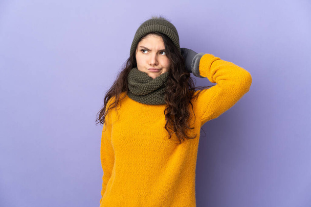 Teenager rusky dívka s zimní klobouk izolované na fialovém pozadí s pochybnostmi - Fotografie, Obrázek