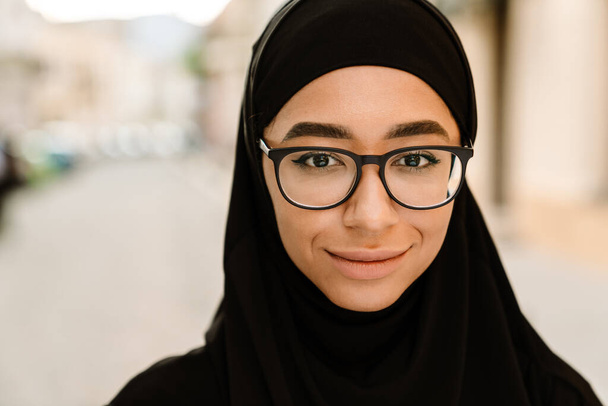 Close up of a smiling young muslim woman in hijab standing on a street - Fotó, kép