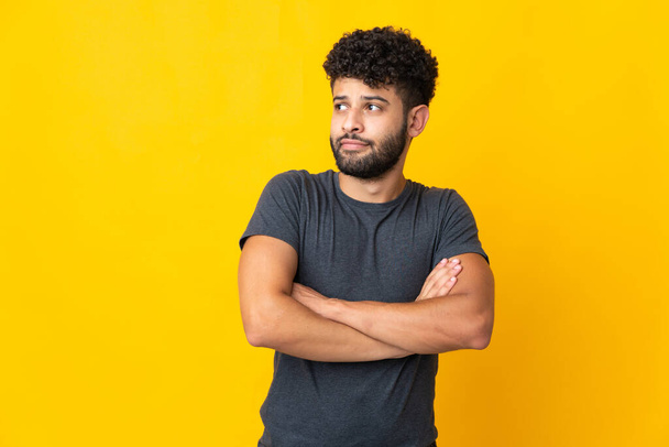 Young Moroccan man isolated on yellow background making doubts gesture while lifting the shoulders - Fotoğraf, Görsel