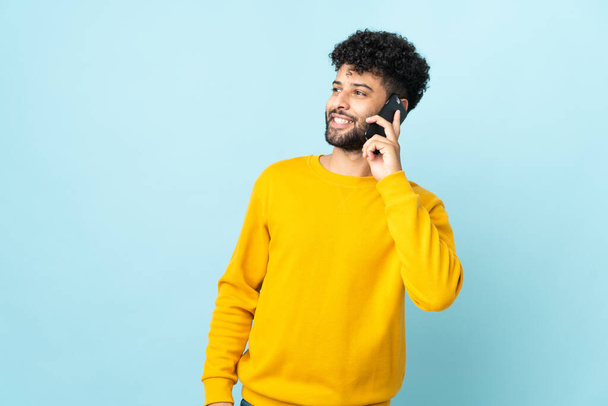 Young Moroccan man isolated on blue background keeping a conversation with the mobile phone - Photo, Image