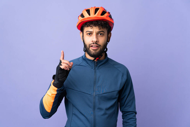 紫の背景に孤立した若いモロッコ人のサイクリストは指を指差すアイデアを考え - 写真・画像