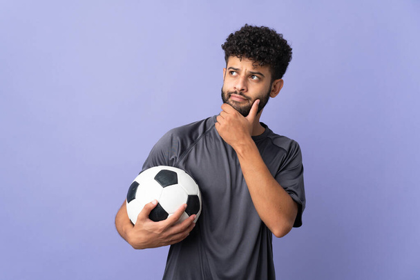 Knappe Marokkaanse jonge voetballer man over geïsoleerd op paarse achtergrond en op zoek omhoog - Foto, afbeelding