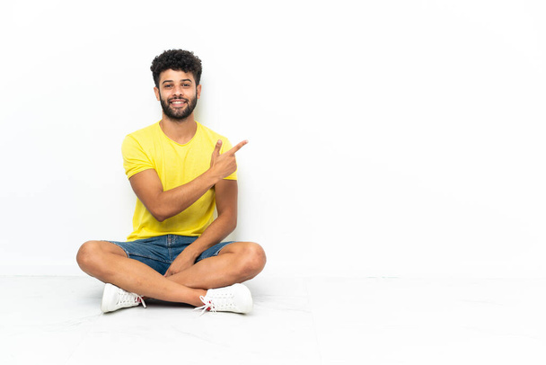 Young Moroccan handsome man sitting on the floor over isolated background pointing back - Photo, Image