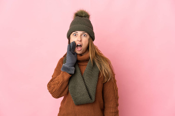 Μέση ηλικία γυναίκα με χειμερινό καπέλο απομονώνονται σε ροζ φόντο με έκπληξη και σοκαρισμένη έκφραση του προσώπου - Φωτογραφία, εικόνα