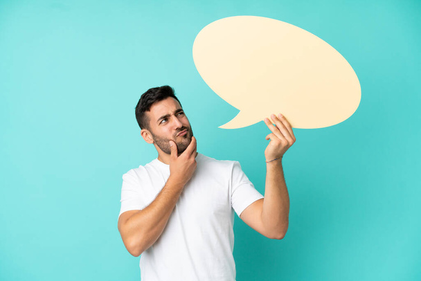 Young handsome caucasian man isolated on blue background holding an empty speech bubble and thinking - Photo, Image