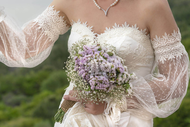 Düğün buketi, gelinin yakın plan eli açık havada çiçek buketi tutuyor. Seçici odaklı ve ses efektli klasik gelinlik giyen bir kadın vücudu. - Fotoğraf, Görsel
