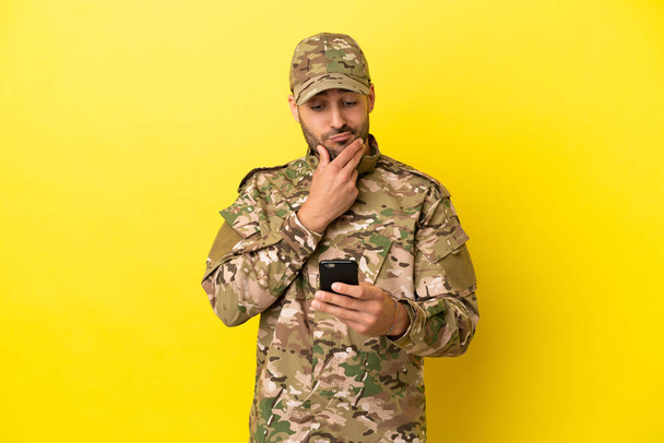 Military man isolated on yellow background thinking and sending a message - Valokuva, kuva