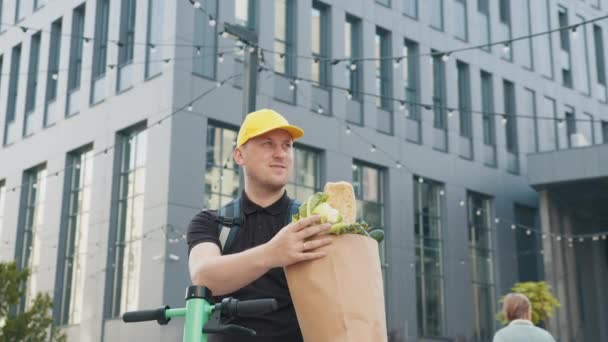 Delivery Concept - Knappe bezorger die pakketdoos met levensmiddelen en drank uit de winkel vervoert. Sluiten op zonlicht koerier in uniform houden verpakking met voedsel. Deur-tot-deur voedselleverancier - Video