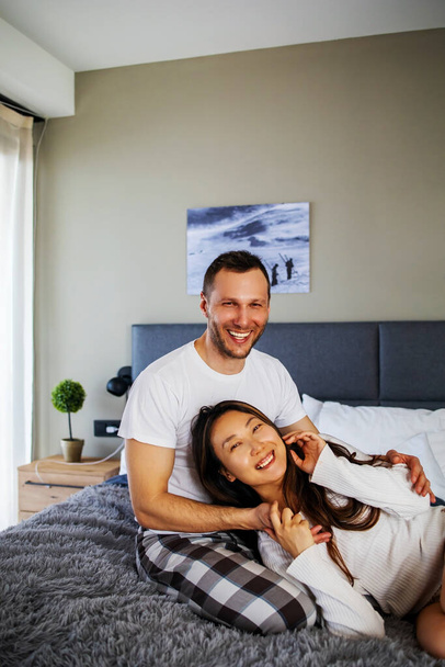 Joven pareja feliz pasar tiempo en casa, sentado en la cama en acogedor apartamento renovado, riendo, divirtiéndose - Foto, imagen