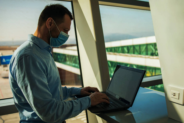 Passagier zakenman dragen maskers covid19 ziektepreventie en Teleconferentie met laptop tijdens het reizen naar het buitenland te werken op de luchthaven terminal. Nieuw normaal en zakenreisconcept - Foto, afbeelding