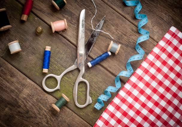 Vintage Background with sewing tools and colored tape. Sewing kit. Scissors, bobbins with thread and needles on the old wooden background - Foto, Imagen
