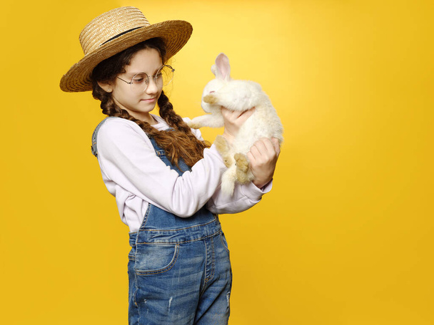 Roztomilý úsměv školačka drží roztomilý skutečný zajíček, izolované žluté pozadí. - Fotografie, Obrázek