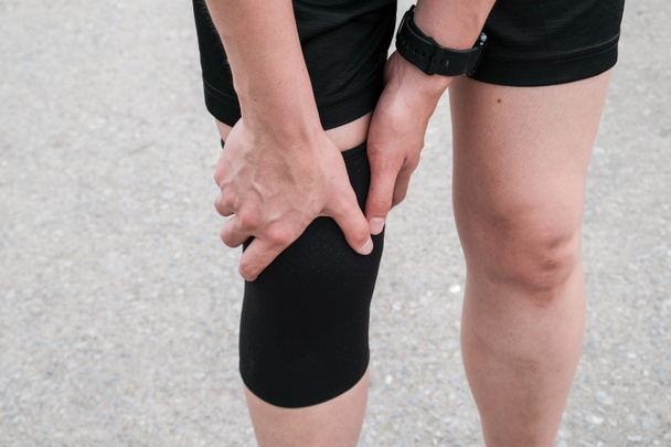 Крупный план бегущей женщины с коленной опорой, чтобы предотвратить и уменьшить боль в колене от бега. Концепция травмы при выполнении тренировки. - Фото, изображение
