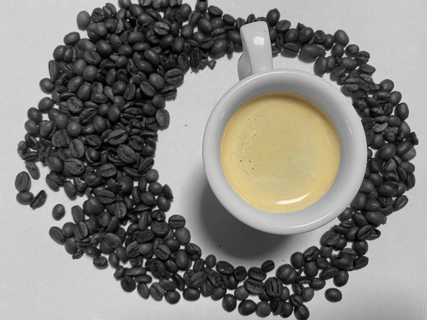 Espresso doré sur tasse en céramique blanche avec grains de café noir et blanc autour de la vue de dessus - Photo, image