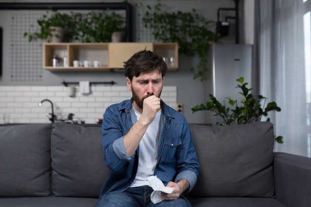 Sick man at home, patient coughing sitting on sofa in kitchen - Foto, afbeelding