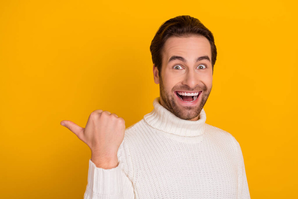 Photo of charming impressed guy wear white pullover pinting back empty space isolated yellow color background - Foto, imagen