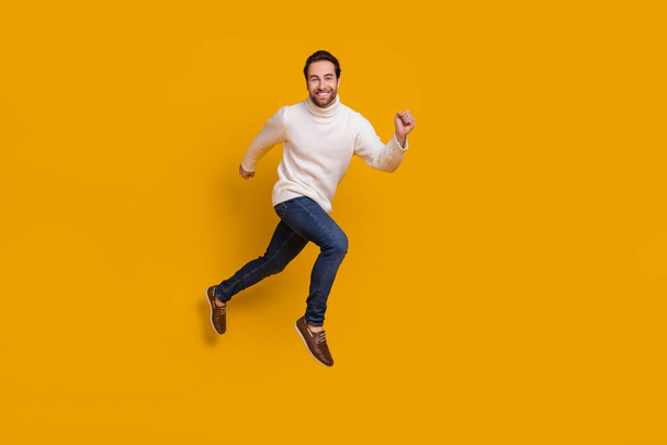 Photo of childish pretty guy dressed white sweater running fast jumping high isolated yellow color background - Fotografie, Obrázek