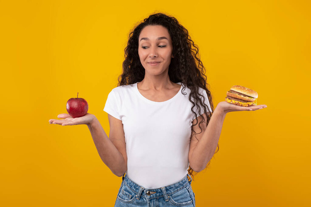 Retrato de senhora sorridente segurando maçã e hambúrguer - Foto, Imagem