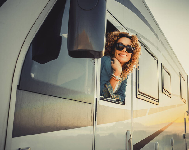 Traveler cheerful and happy expression, beautiful young woman outside the driver window of modern camper van home vehicle. Concept of travel and summer holiday vacation and destination people - Photo, image