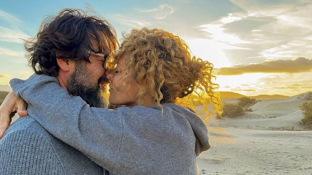 Adult mature happy couple in love kiss with tenderness and sweetness together. Relationship in outdoor leisure activity with man and woman hugging with colored beautiful sunset in background . Travel - Foto, imagen