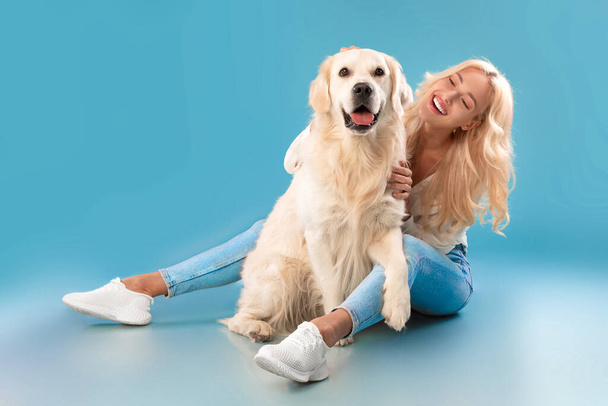 Mujer joven arañando a su perro en el estudio azul - Foto, Imagen