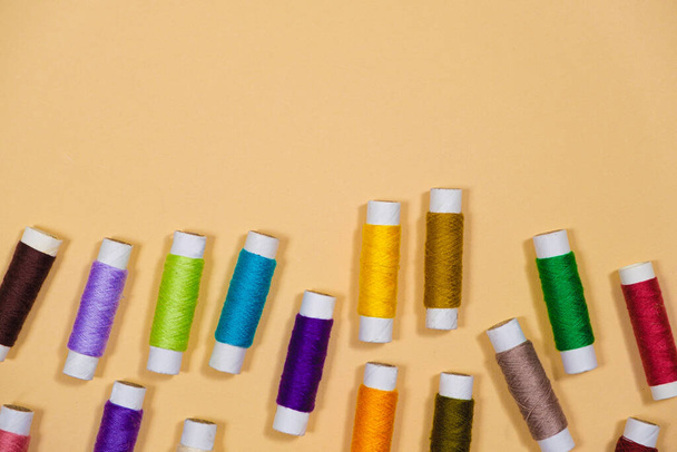 A set of multi-colored threads for sewing with an empty space for text on a beige background, top view. Tailoring and needlework equipment, tailor banner. - 写真・画像