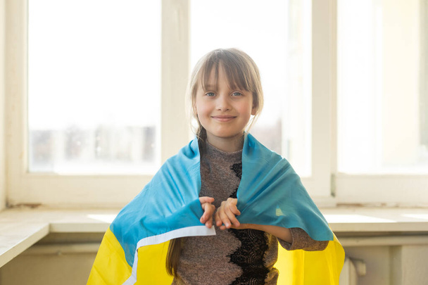 little girl covered with Ukraine flag. Concept of standing with Ukrainian nation in war with Russia. - Foto, Imagen