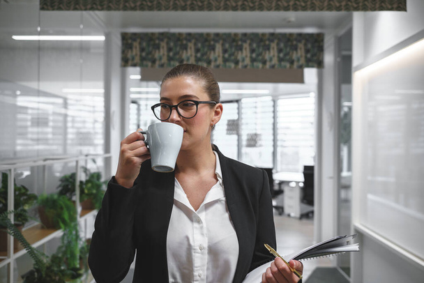Businesswoman drinking coffee in workplace - Photo, Image