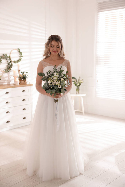 Happy bride wearing beautiful wedding dress with bouquet at home - Foto, afbeelding