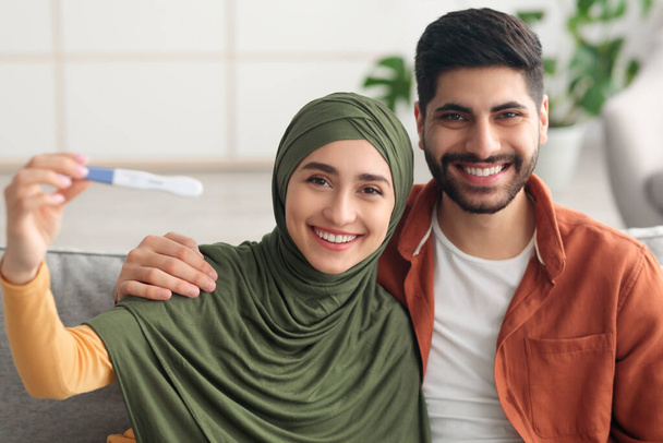 heureux arabe conjoints montrant positif test de grossesse assis à la maison - Photo, image