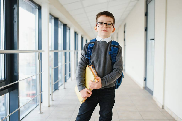 Portrait of happy school student. Smart elementary school kid glasses standing in school. Little child in holding a book. - Photo, image