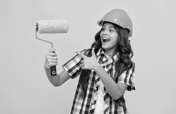 щаслива дівчина-підліток з кучерявим волоссям в будівельному шоломі, вказуючи палець на фарбувальний валик, оновлення
 - Фото, зображення