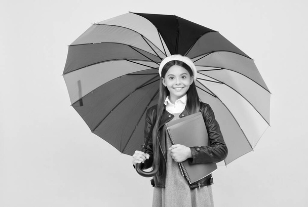 ευτυχισμένη έφηβος κορίτσι κάτω από πολύχρωμη ομπρέλα για την προστασία της βροχής το φθινόπωρο κρατήστε σημειωματάριο, μελέτη. - Φωτογραφία, εικόνα