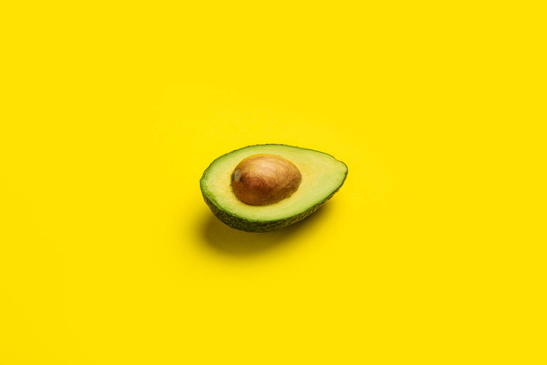 свежая созревшая половина авокадо на ярко-желтом фоне. Вид сверху, плоский. - Фото, изображение