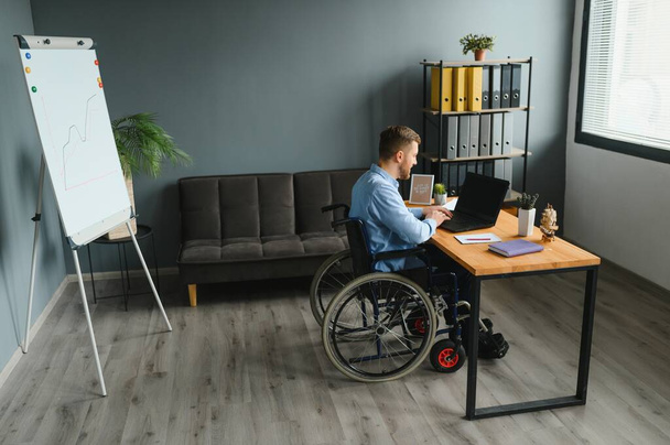 Handicapped Businessman Sitting On Wheelchair And Using Computer In Office - Foto, afbeelding
