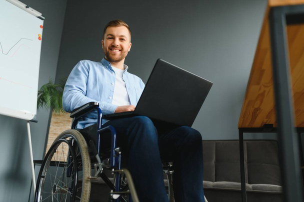 Disabled person in the wheelchair works in the office at the computer. He is smiling and passionate about the workflow. - Foto, immagini