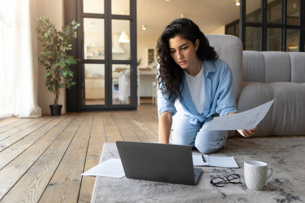 Mujer joven seria que trabaja en el ordenador portátil desde casa, mirando a través de documentos, teniendo reunión de negocios en línea - Foto, imagen