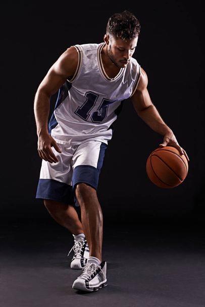 Dribbelen pro. Studio shot van een basketbalspeler tegen een zwarte achtergrond. - Foto, afbeelding