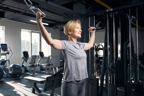 Joyful woman using gym trainer in fitness center - Zdjęcie, obraz