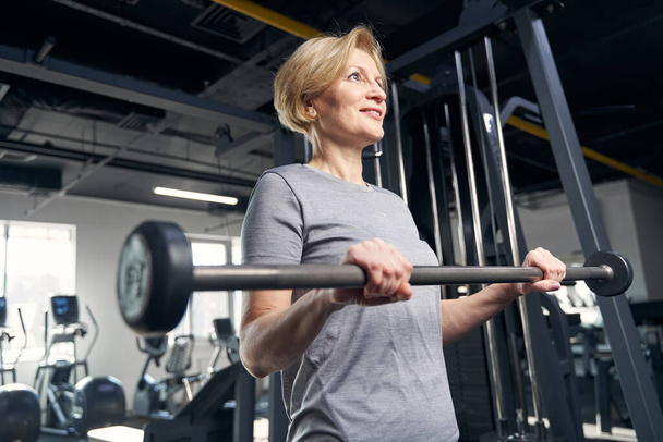 Joyful woman doing exercise with barbell in gym - Foto, Bild
