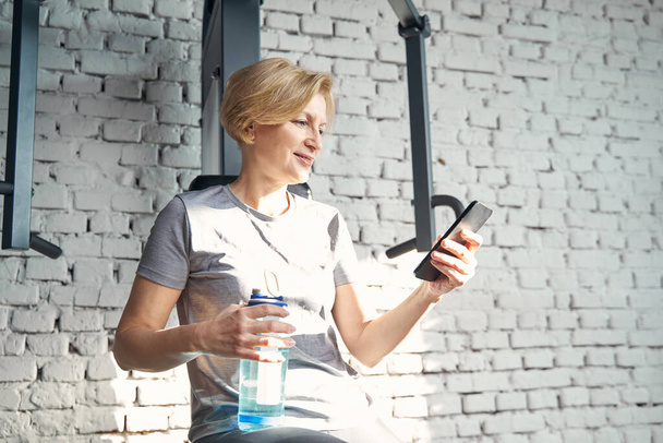 Sporty woman using smartphone in fitness center - Zdjęcie, obraz