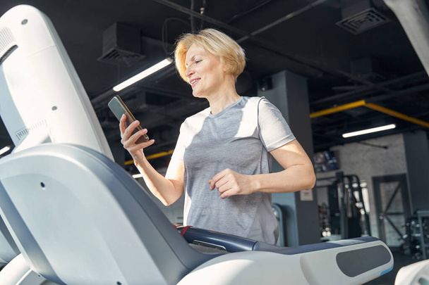 Cheerful woman using cellphone during workout in gym - Foto, afbeelding