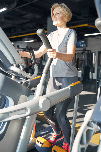 Cheerful woman using cardio stepper machine in gym - Foto, afbeelding