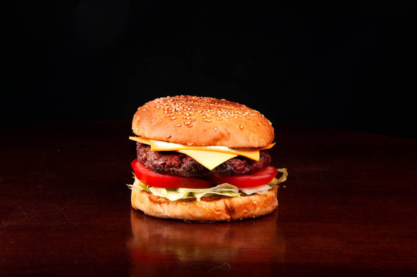 naudanliha hampurilainen pulla seesaminsalaatilla tomaatti cheddar juusto puinen pöytä tummalla pohjalla - Valokuva, kuva