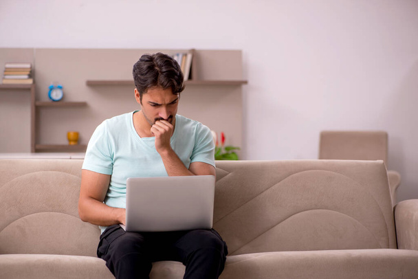 Mladý muž sedí na pohovce s počítačem doma - Fotografie, Obrázek
