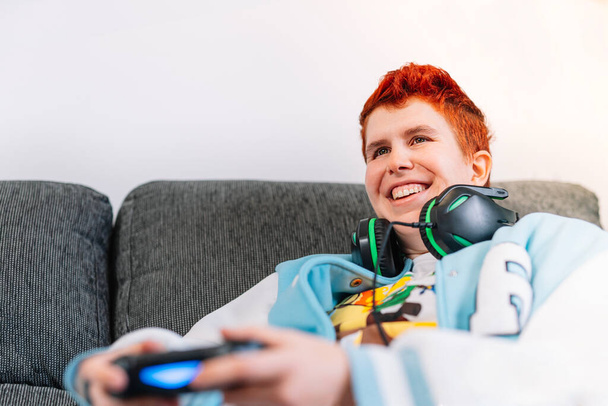 κοντινό πλάνο ενός χαμογελαστού μη δυαδικού ατόμου που παίζει βιντεοπαιχνίδια στο σαλόνι στο σπίτι - Φωτογραφία, εικόνα